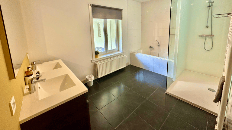Spacious bathroom in a city center eight persons apartment in Bruges with a shower, bath, double sink, hand towels, and toiletries.