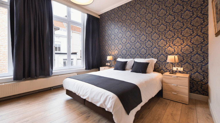 Spacious bedroom in a city center apartment in Bruges with a queen-size bed, large windows, modern furniture, and wooden floors.